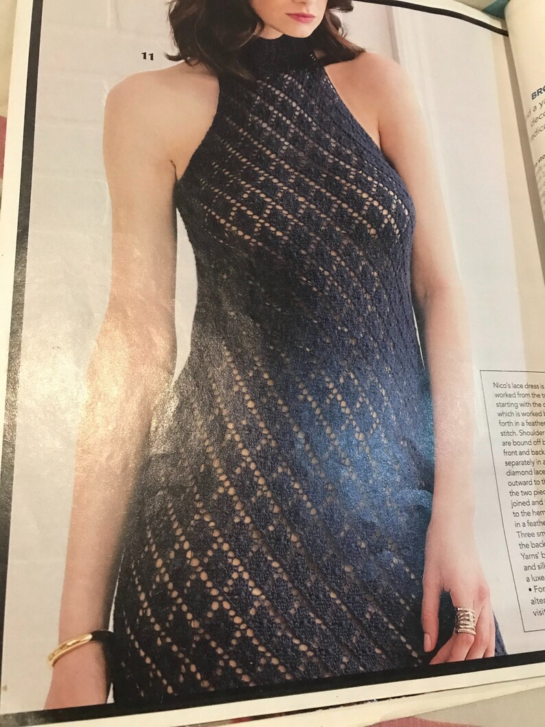 May include: A navy blue, halter-style lace dress with a high neckline. The dress features a diamond-patterned openwork design. The dress is sleeveless and has a fitted bodice that flows into a flared skirt.