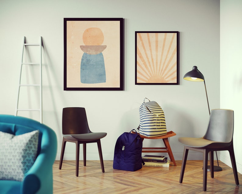 May include: A living room interior with two framed abstract art prints on the wall, a white ladder, two chairs, a blue armchair with a patterned pillow, a floor lamp, and two backpacks on a wooden stool.
