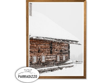 Könnte beinhalten: Ein gerahmter Druck eines schneebedeckten Holzhauses. Die braunen Baumstämme der Hütte kontrastieren mit dem weißen Schnee auf dem Dach und der umliegenden Landschaft. Das Bild ist in einem Holzrahmen, mit dem Text "PARRADIZZO" unten links.