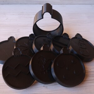 K&ouml;nnte beinhalten: Ein Set aus acht schwarzen Weihnachtsbaumschmuck-Ausstechern aus Kunststoff. Die Ausstecher sind in Form von Ornamenten mit verschiedenen Designs, darunter Schneeflocken, Sterne und ein Schneemann. Ein Ausstecher ist gr&ouml;&szlig;er als die anderen und hat die Form eines traditionellen Weihnachtsbaumanh&auml;ngers.