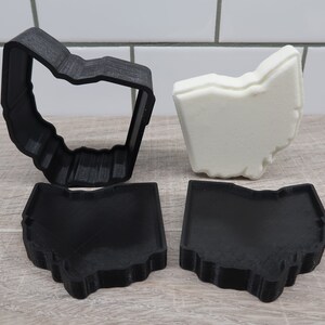 Könnte beinhalten: Ein Set aus drei schwarzen 3D-gedruckten Ausstechern in Form des Bundesstaates Ohio. Ein Ausstecher ist offen, die anderen beiden sind geschlossen.
