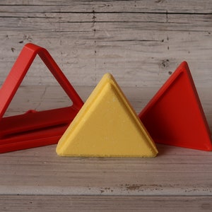 May include: Three triangle-shaped cookie cutters, one red, one yellow, and one red. The cutters are made of plastic and are sitting on a wooden surface.