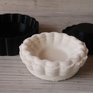 May include: Two round cake pans, one black and one white. The white pan has a fluted edge.