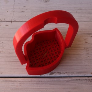 May include: A red plastic 3D printed lip-shaped container with a handle. The container has a patterned design and is empty.