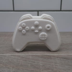 May include: White bath bomb shaped like a video game controller. The controller has buttons labelled A, B, X, and Y.
