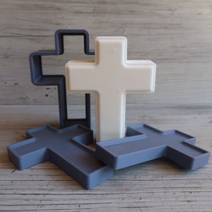 Puede incluir: Tres cruces de madera, una blanca y dos grises, apiladas una encima de la otra. La cruz blanca está en el medio y las cruces grises están a cada lado.