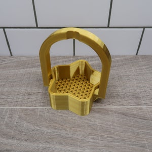 Pode incluir: Uma cesta dourada em forma de estrela com uma alça. A cesta é feita de um material tecido e tem um design decorativo.