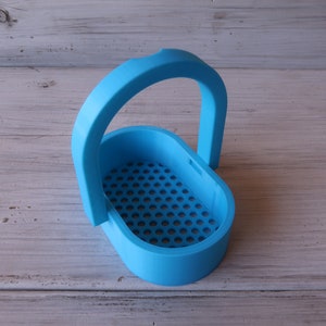 May include: A light blue plastic basket with a handle. The basket has a grid pattern on the bottom.