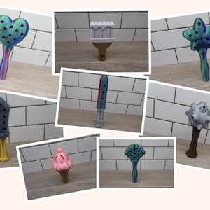 May include: A collection of 3D printed decorative handles with various designs, including a heart, a paintbrush, a star, a sword, a spiked ball, a crown, and a fan. The handles are made of plastic and are painted in various colours.