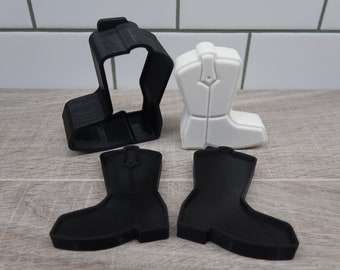 May include: A set of four black and white plastic cowboy boot cookie cutters. The cutters are in two pieces, one for the top of the boot and one for the bottom.