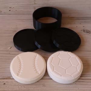 May include: Four black and white silicone molds for making soap or candles. Two molds are shaped like baseballs and two are shaped like soccer balls.