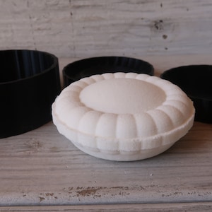 May include: A white round decorative box with a raised design, surrounded by three black silicone molds.