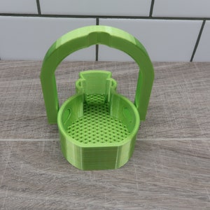 May include: A green 3D printed basket with a handle. The basket has a mesh bottom and is designed to hold small items.