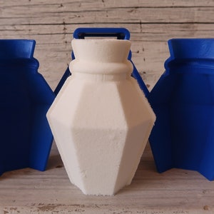 May include: A white, geometrically shaped bottle mould with two blue plastic moulds on either side. The moulds are open and ready to be used.