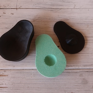 May include: Three avocado-shaped containers, one black, one green, and one black with a small black knob on top. The containers are on a light wood surface.