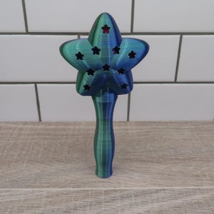 May include: A blue and green star-shaped wand with a handle. The star has a pattern of smaller stars cut out of it.
