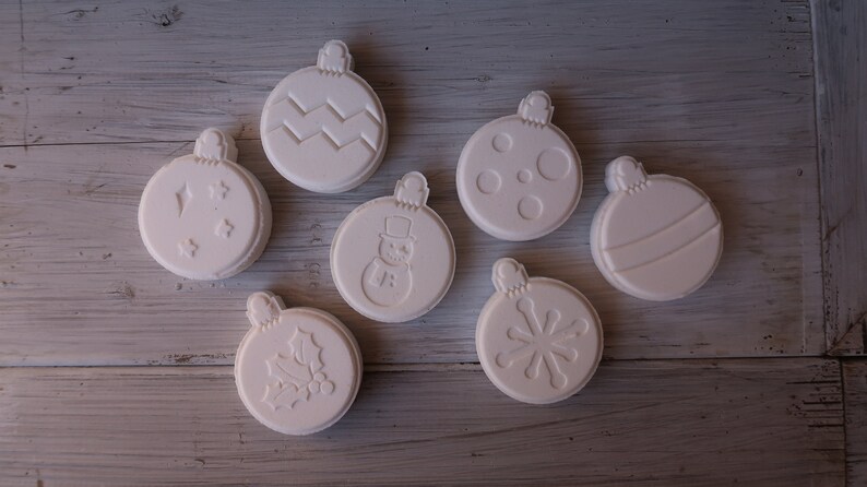 K&ouml;nnte beinhalten: Sieben wei&szlig;e Keramik-Weihnachtskugeln mit verschiedenen Designs, darunter ein Schneemann, eine Schneeflocke, Stechpalme und ein Zickzackmuster.