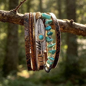 May include: A multi-strand bracelet featuring a silver-toned metal feather charm with a central turquoise stone, strands of brown leather, snakeskin-patterned leather, and a string of irregular turquoise beads accented with small silver-toned metal beads.