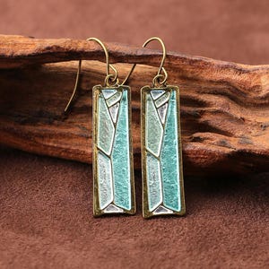 May include: A pair of rectangular drop earrings featuring an antique brass frame with a geometric inlay of textured light blue and silver enamel segments. Each earring hangs from a simple brass hook, showcasing a segmented mosaic-like pattern.
