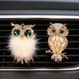 Peut inclure: Deux clips de désodorisant de voiture en forme de hibou. Le hibou de gauche présente une monture en métal doré, des yeux en cristal vert et un corps en fausse fourrure blanche. Celui de droite est en métal doré avec des yeux en cristal vert.