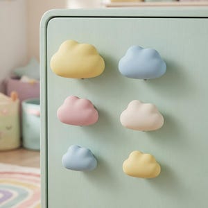 May include: A light green cabinet door features six cloud-shaped knobs arranged in two vertical columns. The knobs are colored in soft pastel shades of yellow, blue, pink, and cream, providing a smooth, rounded surface for opening drawers.