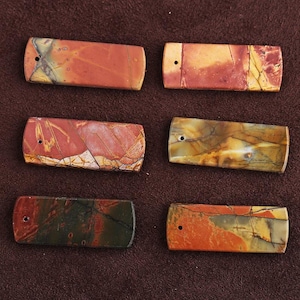 Puede incluir: Seis cuentas rectangulares de piedra en tonos rojos, naranjas, amarillos y verdes. Cada cuenta tiene un patrón único y un pequeño agujero perforado en un extremo. Las cuentas son lisas y pulidas, ideales para la creación de joyas.