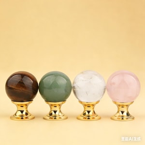 May include: Four crystal spheres in brown, green, clear, and pink, each mounted on a gold-coloured base. The spheres are arranged in a row against a light yellow background.