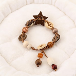 May include: A handcrafted bracelet with a star-shaped charm and an assortment of wooden beads and buttons in brown, beige, and cream tones. The bracelet is strung on a brown cord and has a dangling charm.