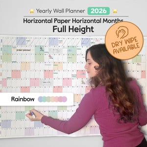 May include: A large, rainbow-coloured 2026 yearly wall planner with horizontal months. The planner is full height and has a dry-wipe surface. The image shows a person using a marker on the planner.