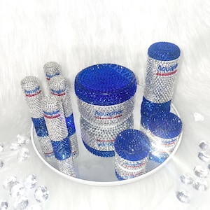 以下が含まれることがあります： ラインストーンが付いた青と銀の容器5個セット。容器は鏡面トレーの上に置かれています。容器には「Aquaphor」の文字が書かれています。