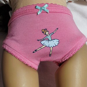 May include: Pink underwear with a light blue bow and a ballerina graphic. The underwear has a scalloped edge and a cartoon ballerina in a blue tutu. The underwear is made of a soft, ribbed fabric.