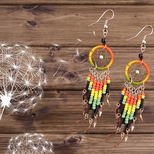 May include: A pair of dangle earrings with a dreamcatcher design. The earrings are made with colorful beads in shades of green, yellow, orange, and black. The dreamcatchers are silver with a green and yellow beaded border.