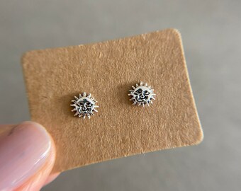 May include: A pair of silver earrings with a sun design. The earrings are on a brown card.