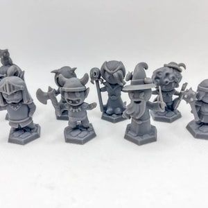 Peut inclure: Ensemble de figurines miniatures grises représentant des personnages fantastiques, dont un chevalier avec une épée, un gobelin avec une hache et un magicien avec un bâton. Chaque figurine est sur une base hexagonale.
