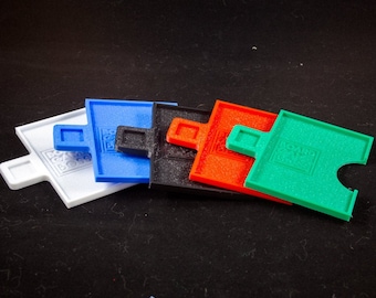 May include: Five plastic puzzle pieces in different colors: white, blue, black, orange, and green. Each piece has a raised square with the word "LEGO" printed on it.