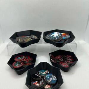 May include: Five black hexagonal plastic trays containing various circular and square game tokens. The tokens feature printed illustrations of characters, text labels such as Wound, Townfolk, and Zombie Here, and dark, colorful graphic designs.