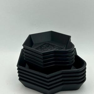 May include: A stack of black, hexagonal-shaped trays designed for organizing game components. The top tray features the embossed text "BOARD GAME ACCESS" on its base. Each tray has raised edges and a uniform, matte finish, creating a compact set.
