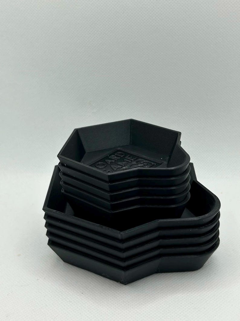 May include: A stack of black, hexagonal-shaped trays designed for organizing game components. The top tray features the embossed text "BOARD GAME ACCESS" on its base. Each tray has raised edges and a uniform, matte finish, creating a compact set.