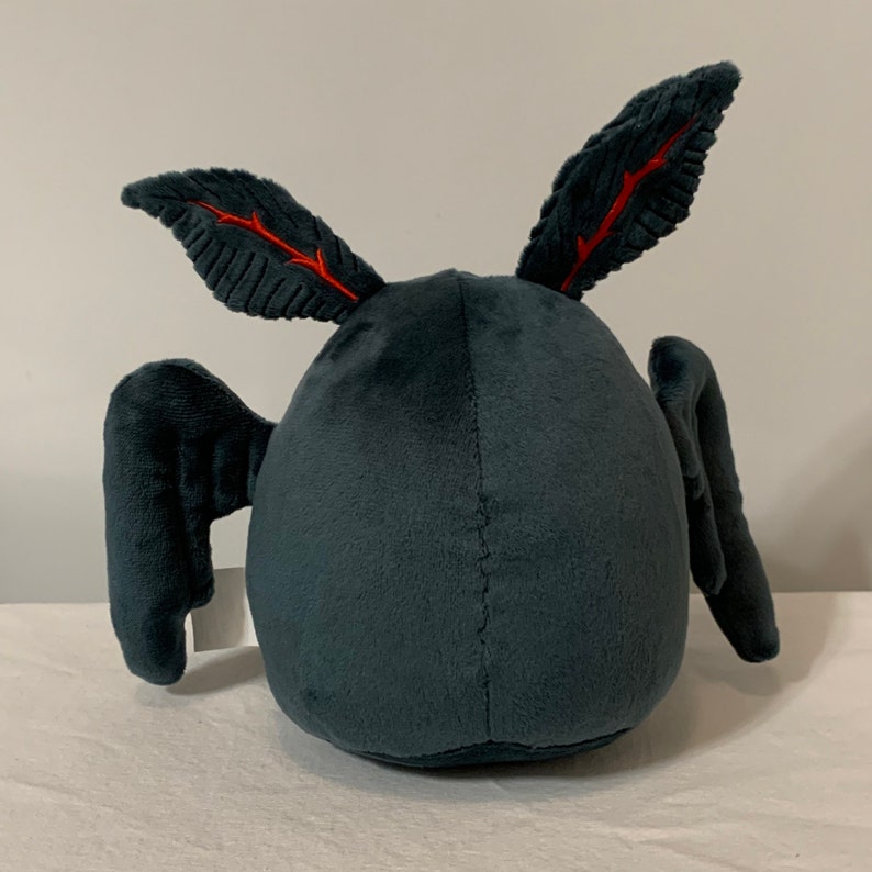 May include: A plush gray bat with red veins on its wings. The bat is sitting on a white surface.