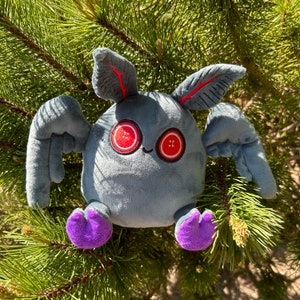 May include: A gray plush toy with large red eyes and purple feet. The toy has wings and a long, thin body.