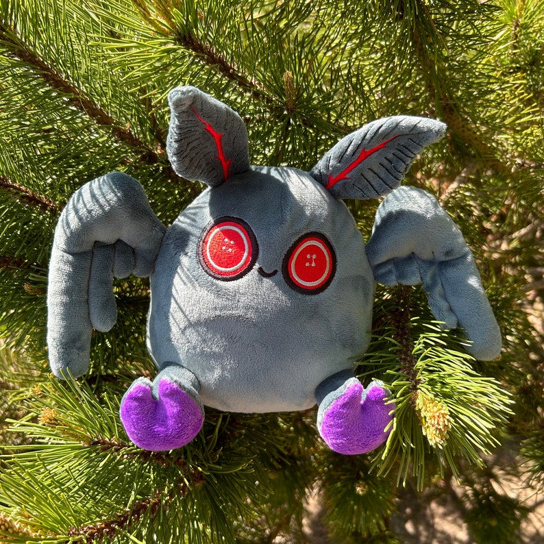 May include: A gray plush toy with large red eyes and purple feet. The toy has wings and a long, thin body.