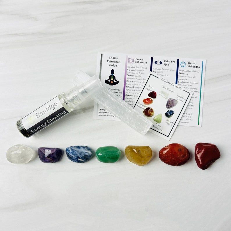 Pu&ograve; includere: Un set di sette cristalli di chakra, ognuno di un colore diverso, disposti in fila su una superficie bianca. I cristalli sono etichettati con i loro nomi e colori di chakra corrispondenti. C'&egrave; anche una bottiglia di spray per la pulizia energetica e un bastoncino di selenite.