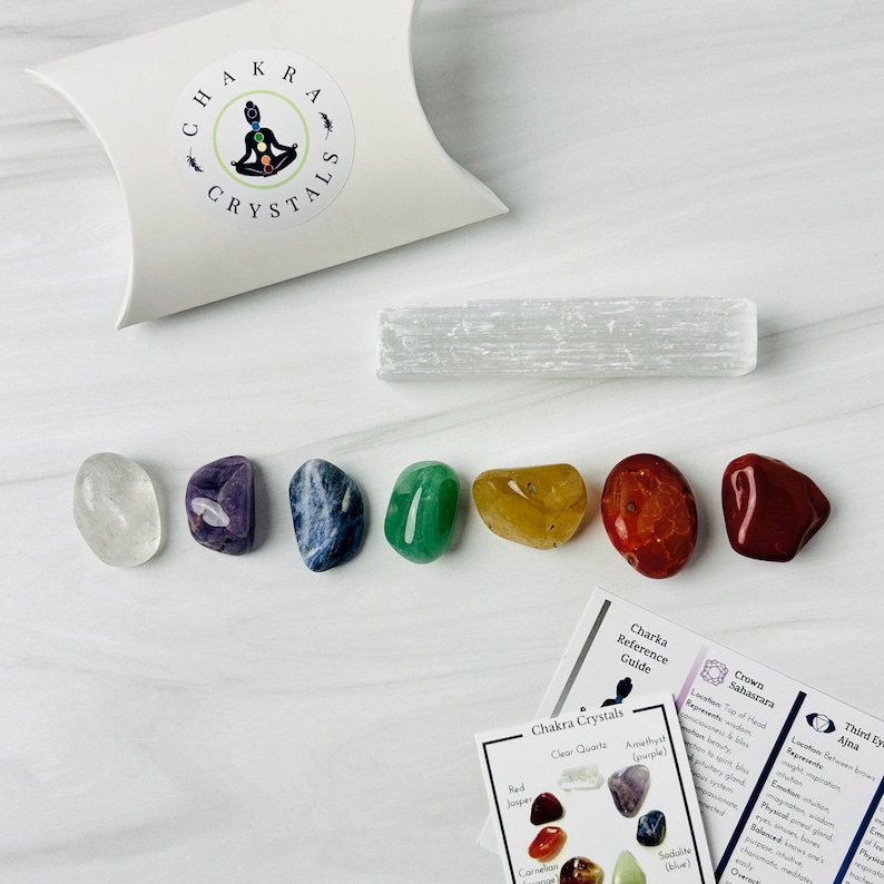 Pu&ograve; includere: Set di sette cristalli chakra, tra cui quarzo trasparente, ametista, sodalite, aventurina verde, citrino, corniola e diaspro rosso. I cristalli sono disposti a forma di arcobaleno su una superficie bianca. Sono inclusi anche una bacchetta di ricarica in selenite e una carta con informazioni sui chakra.