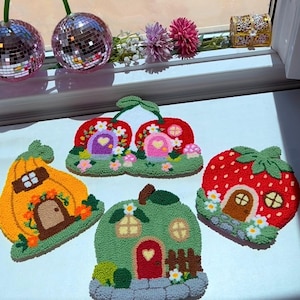 May include: Four tufted textile wall hangings shaped like whimsical fruit houses. One is a yellow pumpkin house, one is a green apple house, one is a red strawberry house, and one is a double cherry house with two purple and pink doors.
