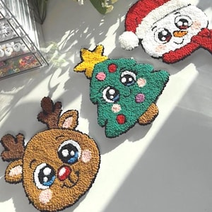 May include: A selection of handmade Christmas decorations with a textured finish. The decorations include a reindeer, a Christmas tree with a yellow star, and a snowman wearing a Santa hat. Each ornament features large, cartoon-style eyes and is made using a looped yarn technique.