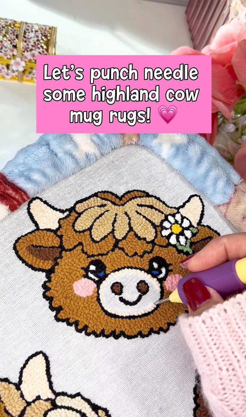 May include: A Highland cow mug rug is being punch needled. The rug features a brown cow face with a flower and the text "Let's punch needle some highland cow mug rugs!" on a pink background.
