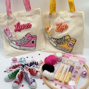 Puede incluir: Dos bolsas de mano de color crema con asas rosas y amarillas, cada una con un diseño de zapatilla bordada de colores y un nombre. También hay llaveros de zapatillas en miniatura y una colección de zapatillas en miniatura de colores, junto con materiales de manualidades.