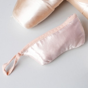 Może przedstawiać: Różowa satynowa torba na buty do baletu ze sznurkiem do ściągania. Torba wykonana jest z miękkiej, lekkiej tkaniny i idealnie nadaje się do przechowywania i przenoszenia butów do baletu.