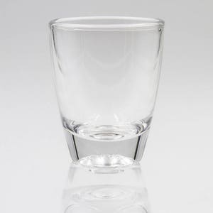May include: A clear, empty glass with a rounded top and a slightly flared base. The glass is made of transparent material, reflecting light and creating a subtle shadow. The design is simple and modern, suitable for various beverages.