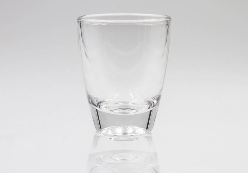May include: A clear, empty glass with a rounded top and a slightly flared base. The glass is made of transparent material, reflecting light and creating a subtle shadow. The design is simple and modern, suitable for various beverages.